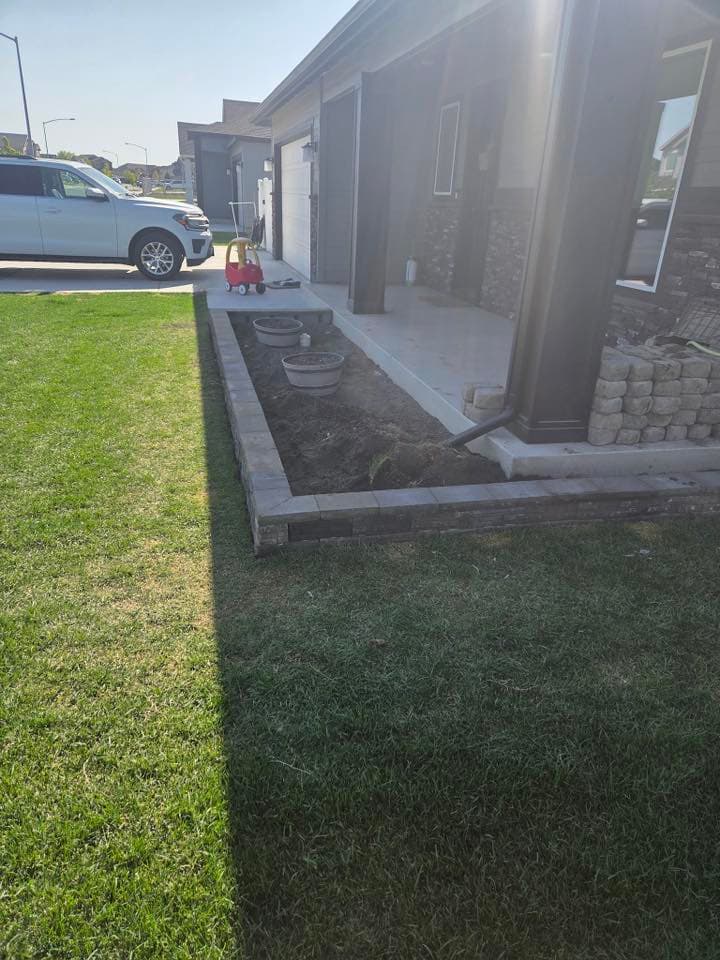 New landscaping with garden bed and pavers next to a house and parked car.